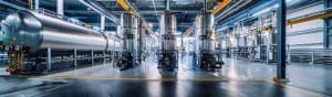 A modern, industrial facility features large, metallic tanks and elaborate piping systems. The space is well-lit, showcasing a clean and organized environment with polished floors and various machinery.