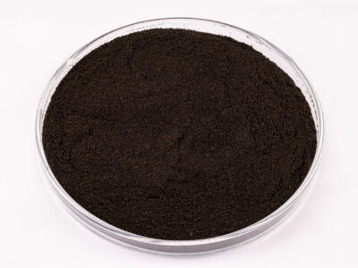 A clear petri dish filled with a fine, dark brown or black powder, placed on a white background.