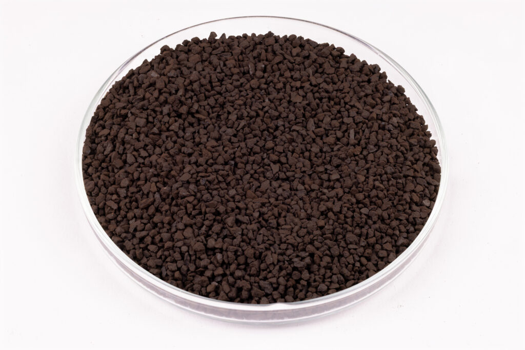 A round, clear petri dish filled with small, dark brown granular pellets is shown on a white background.