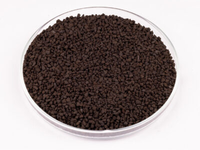 A round, clear petri dish filled with small, dark brown granular pellets is shown on a white background.