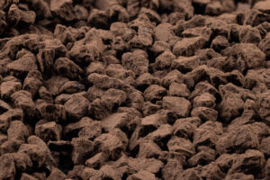 Close-up of many irregular, jagged brown pieces, resembling chunks of chocolate or cocoa powder-coated candy, tightly packed together and filling the entire frame.