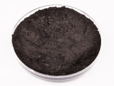 A clear, shallow petri dish filled with a fine, dark black powder sits on a white background.
