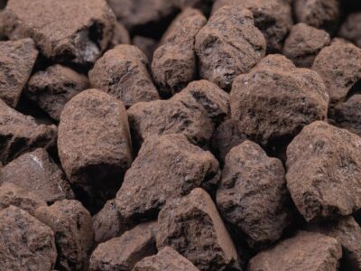 A close-up view of a pile of irregularly shaped, brown porous rocks or chunks, with rough, uneven surfaces and natural texture.
